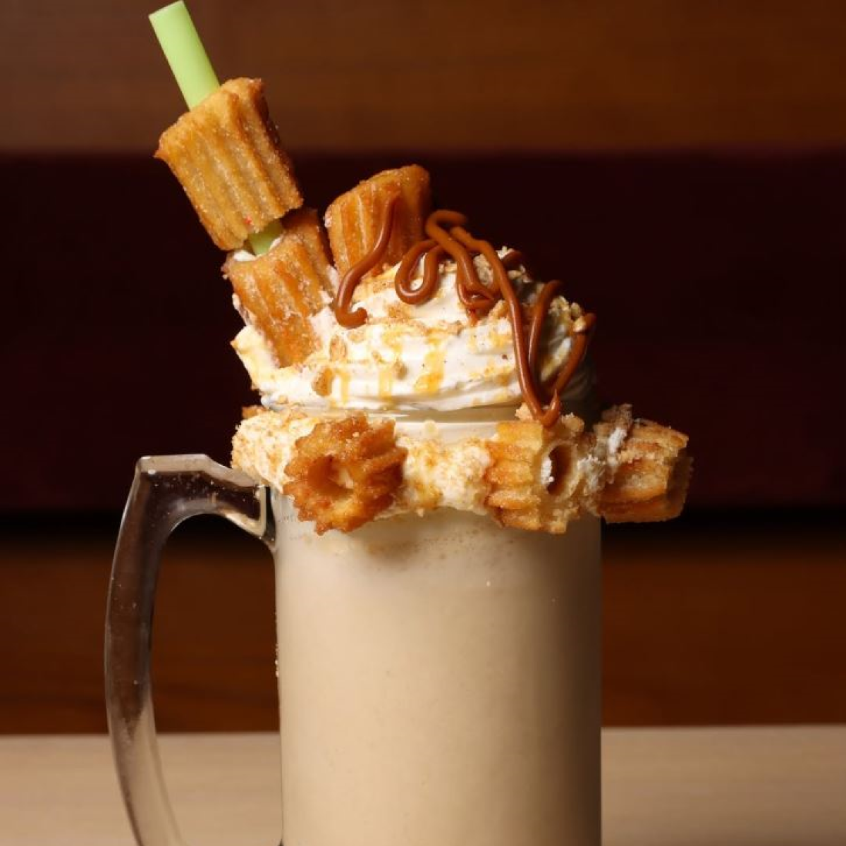 Factoria de Azucar milkshake topped with whipped cream, caramel, and churros in a glass mug.