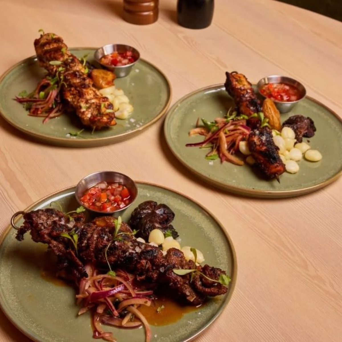 Three green plates of Peruvian entrees with sauces and sides at Factoria de Azucar.