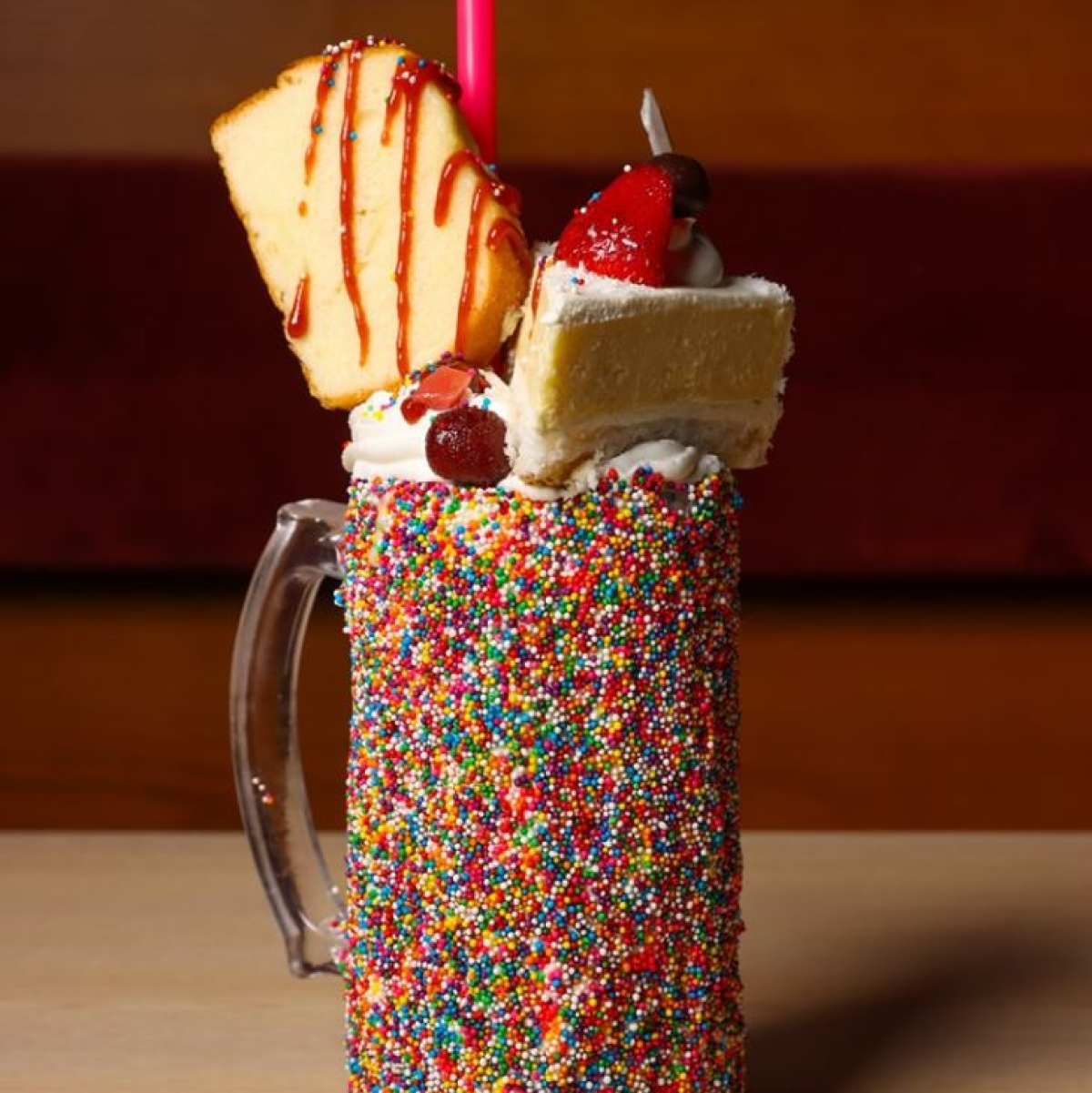 Factoria de Azucar milkshake topped with whipped cream, pound cake, and strawberry cake in a glass mug covered in rainbow sprinkles.